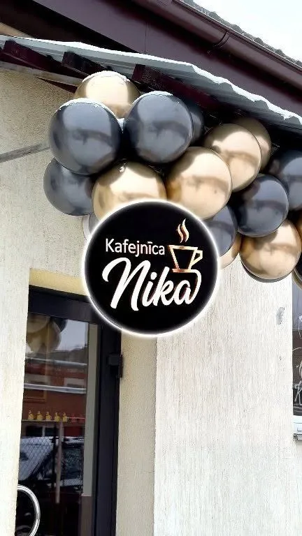 Kafejnīcas Nika ieeja ar melnu, apaļu izkārtni un baloniem virs durvīm